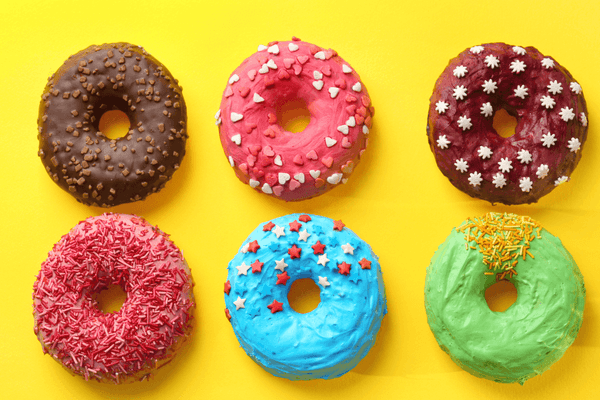 different flavoured donuts with different sprinkles laying on a yellow background